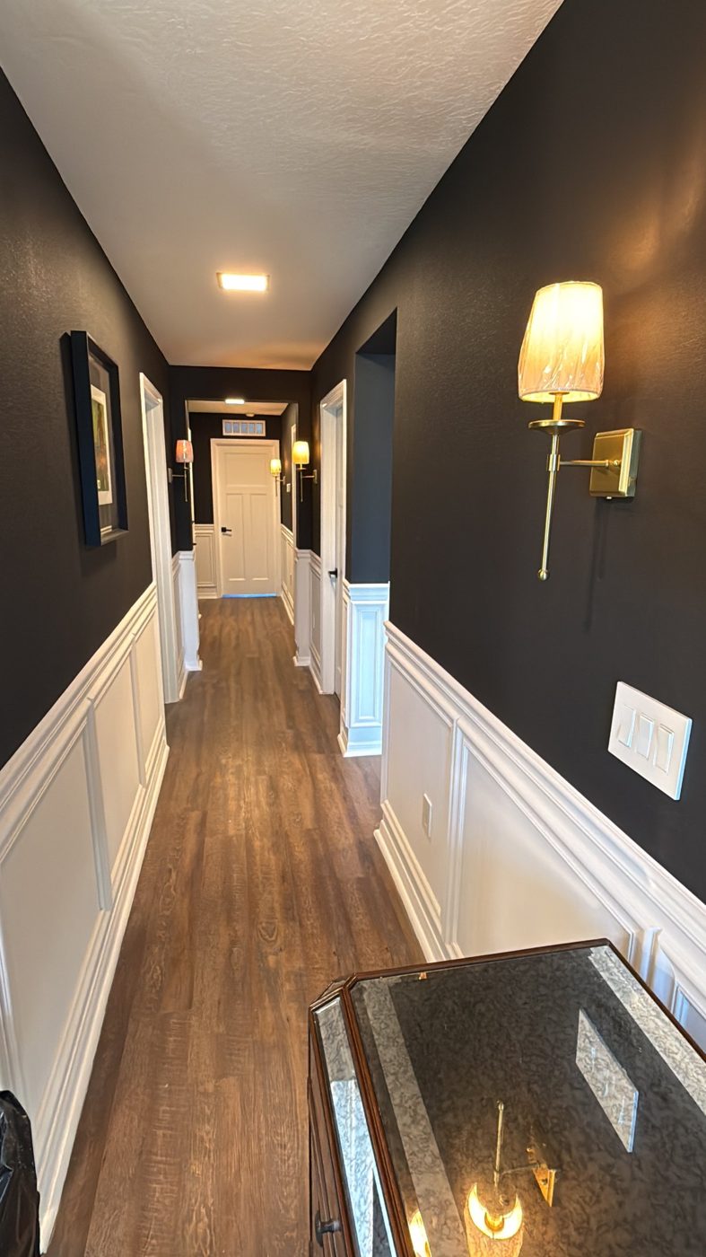 Hallway painted in deep charcoal with white wainscoting and brass sconces